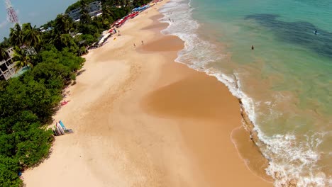 Dron-Aéreo-Sobre-El-Popular-Destino-Turístico-Frente-A-La-Playa-En-Sri-Lanka,-Panorámico-Sobre-La-Gente-En-La-Arena-En-Un-Día-Soleado