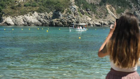 young woman is filming a boat docking on the beach