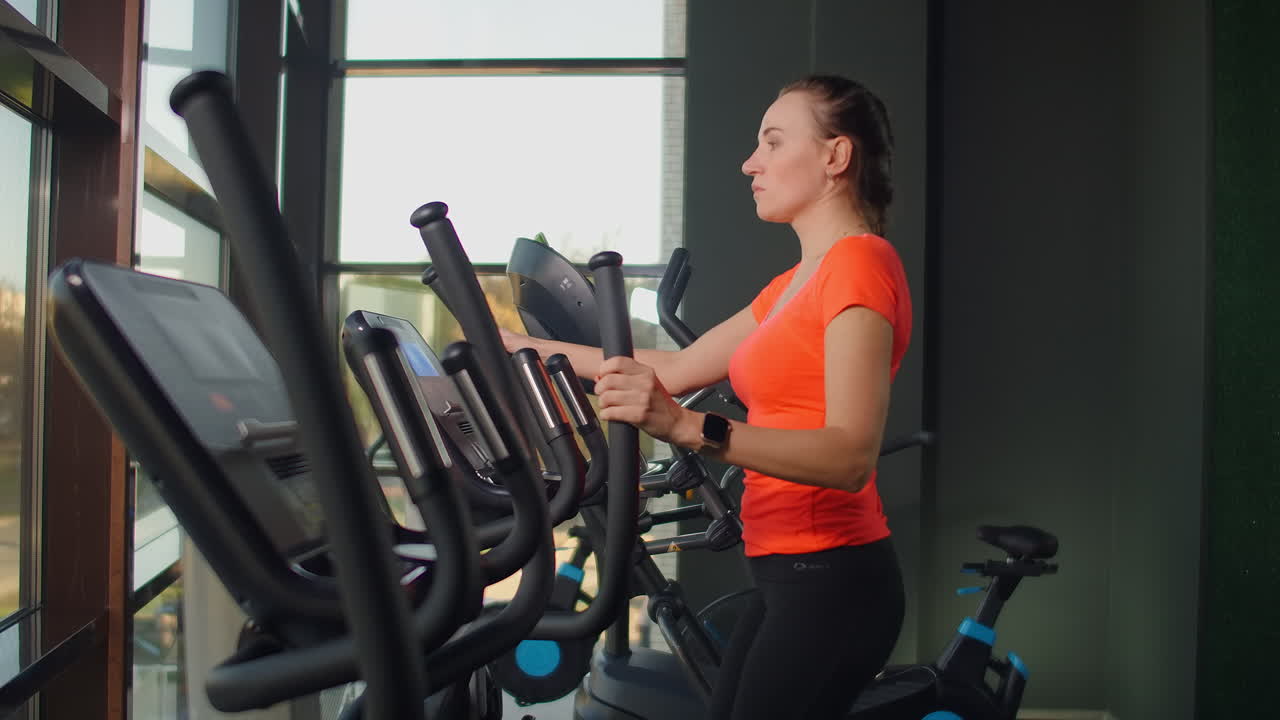 Beautiful fit sportive positive young woman in gym doing exercises on elliptical trainer working out