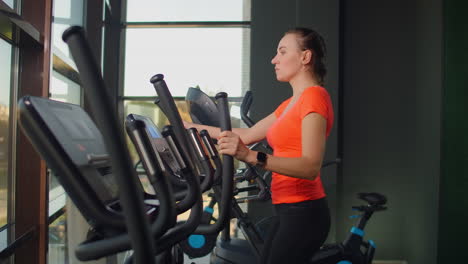 beautiful fit sportive positive young woman in gym doing exercises on elliptical trainer working out