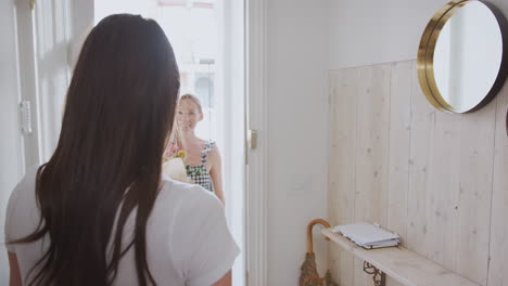 mujer abriendo la puerta de entrada a un compañero gay en casa que le da un ramo de flores