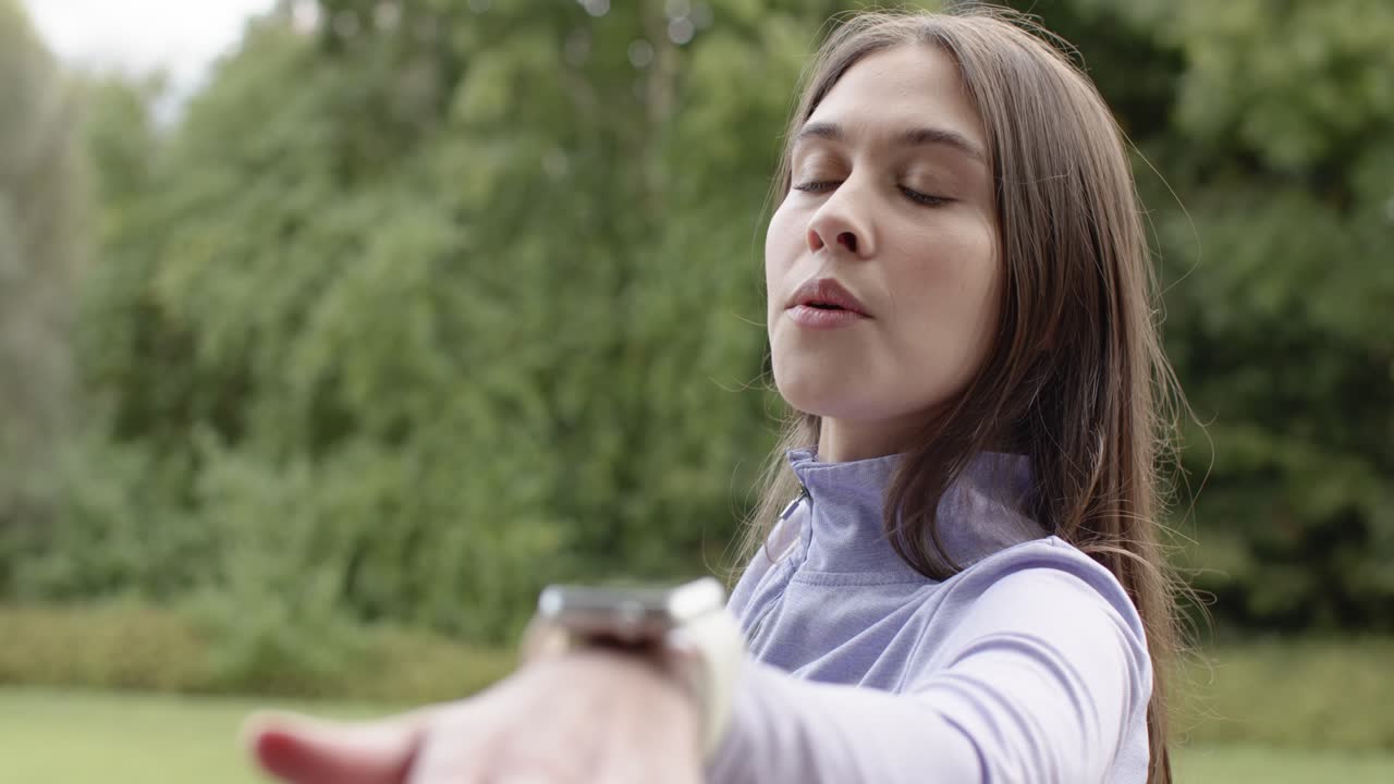 Dopo aver ricevuto un prompt dallo smartwatch, donna ispanica che allunga il braccio destro e inspira durante l'allenamento in uno spiazzo