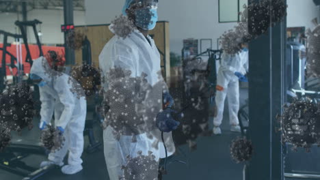 covid-19 cells floating against team of health workers spraying disinfectant at gym