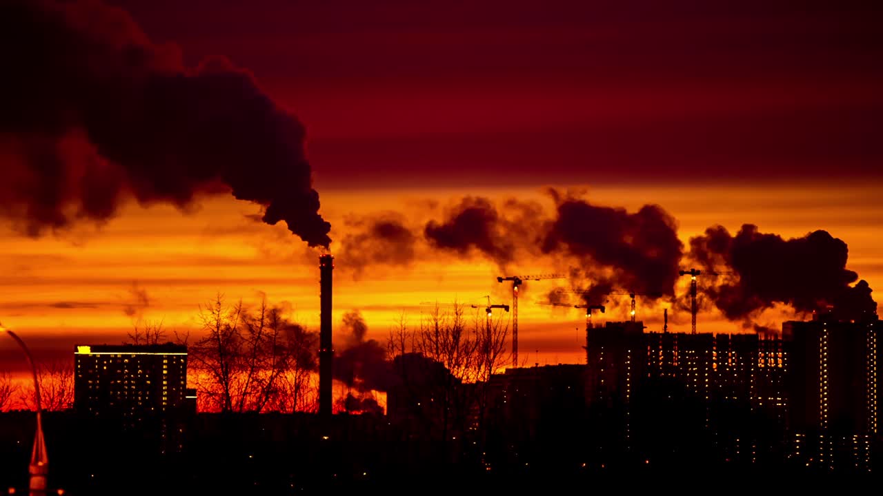 해가 지는 저녁에 현대적인 도시. 파이프에서 연기가 나옵니다.