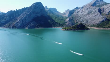 drone capture of small moving vessels on lake riaño and the mountain chain background in spain