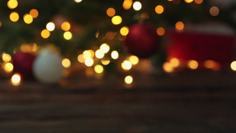 desdibujado árbol de navidad desenfocado luces doradas parpadeantes mano poniendo caja de regalos roja