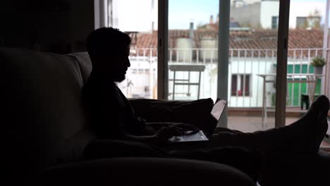 silhouette of ethnic man working on laptop at home