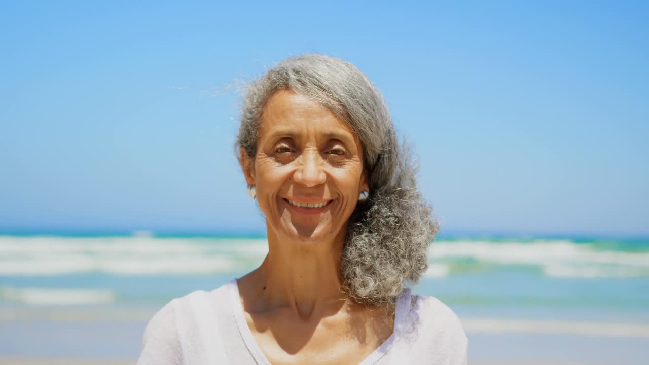 Front view of happy active senior African American woman standing on beach in the sunshine 4k
