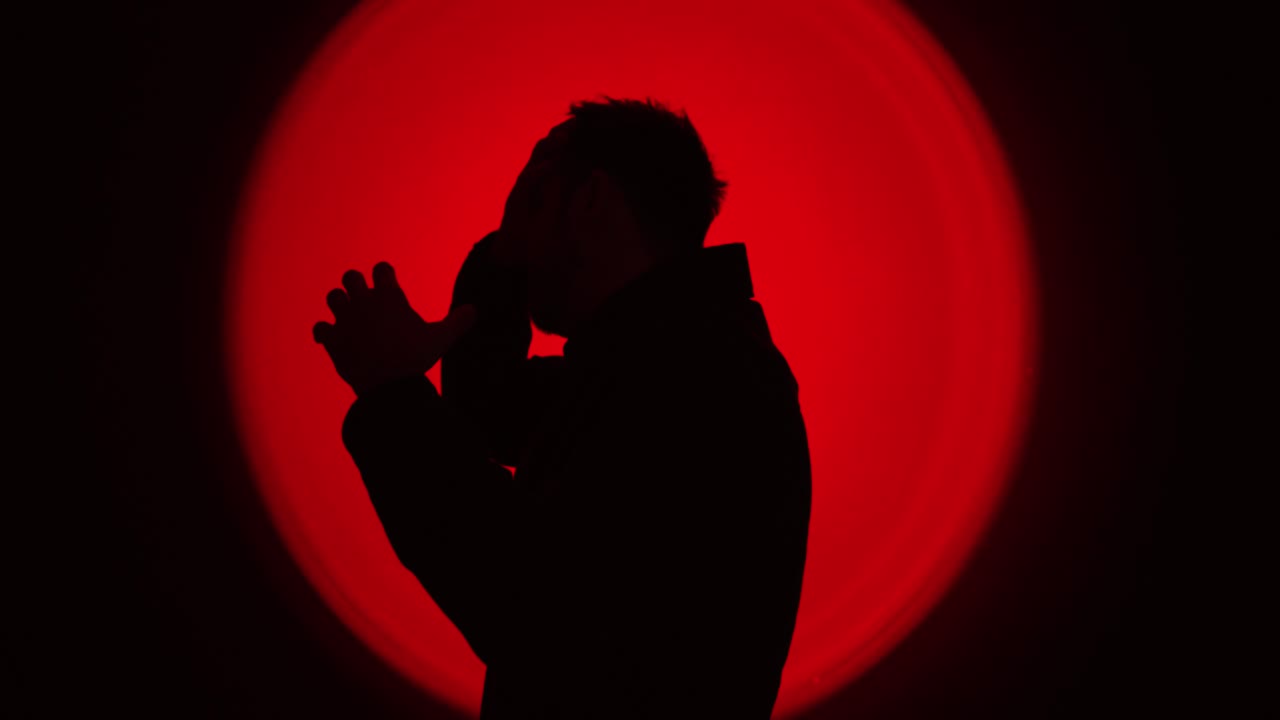 Dramatic silhouette of a man raising clenched fists in anger against a powerful red circular backlight, creating an intense emotional atmosphere. Ideal for concepts like rage, conflict, stress, emotio