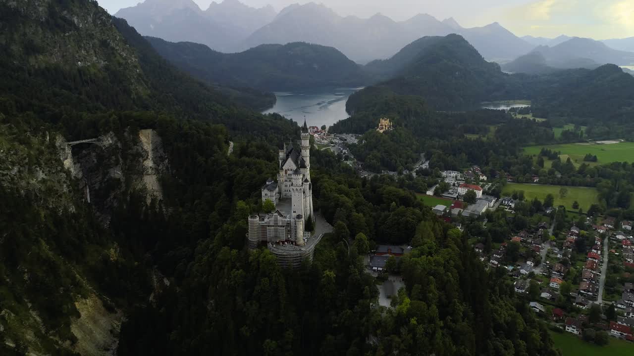 Beutiful aerial around the famous castle Neuschwanstein front revealing the alp mountains behind it and castle Hohenschwangau + lake Alpsee in the background