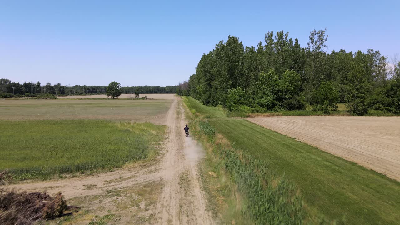 disparo de drones de un adulto joven acelerando a través de una granja en una bicicleta de tierra