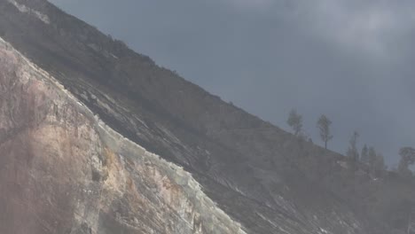 sheer steep rock wall of volcano crater with light clouds from sulfur fumes, aerial