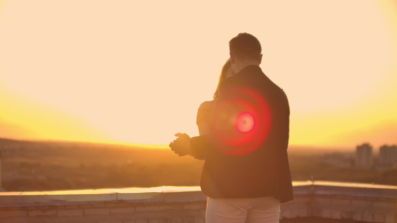 Two lovers a man and a woman laugh and dance on the roof at sunset. Slow motion happy couple summer on the roof.