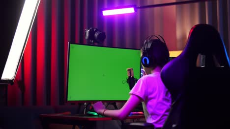 vista trasera de la chica asiática streamer gritando gol y bailando celebrando el juego ganador en la computadora de pantalla verde. videojuego de transmisión en vivo, escritorio iluminado por luz de tira de led rgb
