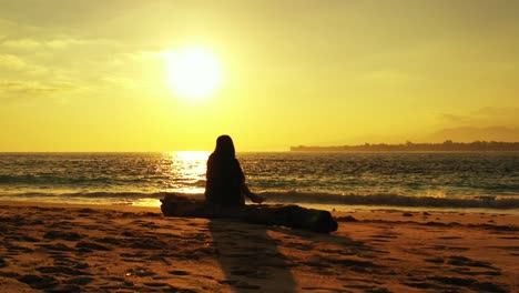 Chica-Disfrutando-De-Una-Hermosa-Puesta-De-Sol-Con-Un-Cielo-Naranja-Amarillo-Reflejado-En-La-Superficie-Del-Mar-Sentada-En-Una-Playa-Exótica-En-Indonesia