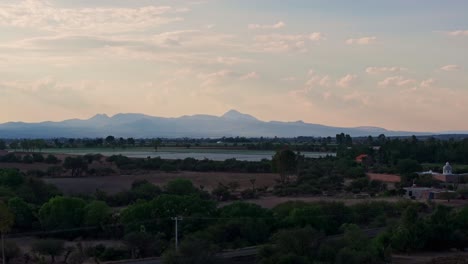 Paso-Elevado-Aéreo-Sobre-Las-Afueras-De-La-Granja-Rural-Y-Los-Campos-Bajo-El-Anochecer-De-La-Hora-Azul