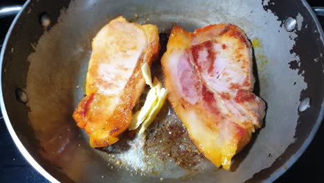 Sizzling-back-bacon-chops-frying-in-butter-and-olive-oil-in-a-steel-pan-on-glass-stove-top