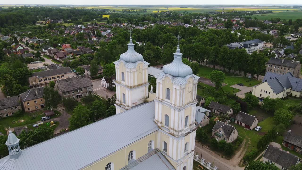 Baroque-style Lithuanian church towers rise above village homes, orbiting drone