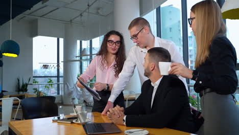 discussing ideas and collaborating at work. office people gathered around man sitting at the desk and talk looking at the papers.