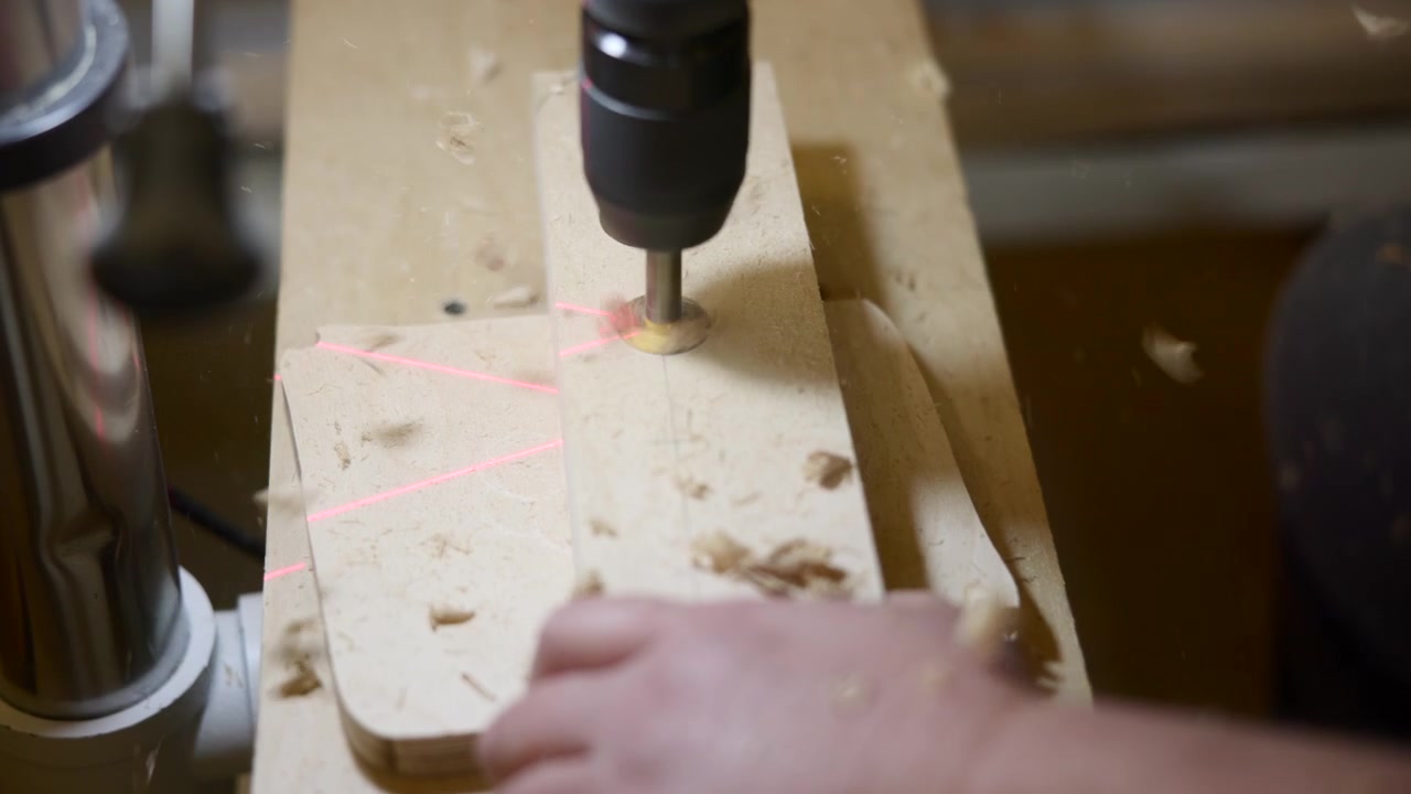 Guia a laser marcando posições de furos em peça de madeira, broca alinhando-se com linhas vermelhas brilhantes, mão gentil. Mídia