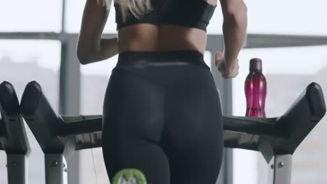 Back-view-sport-woman-training-leg-flexion-at-treadmill-in-fitness-gym.