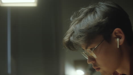 focused young man with earbuds and glasses in a dimly lit room