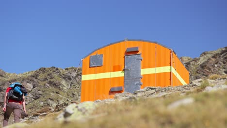 solo male hiking up to bright orange bothy on mountainside in valmalenco