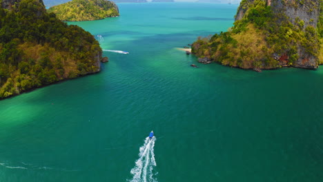drone-following-longtail-boat-driving-towards-small-green-islands,-aerial