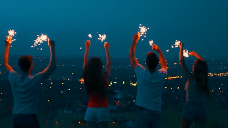 the four people holding sparklers lights on the top of the hill. slow motion