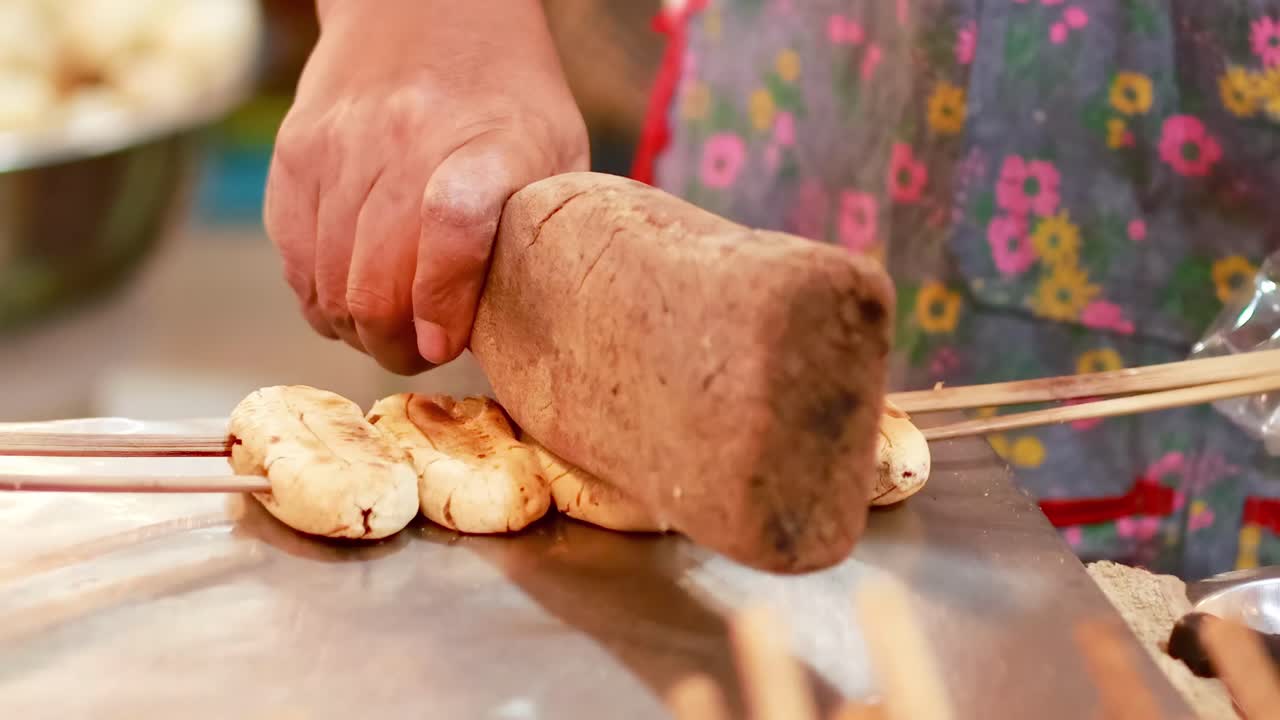 Close-up of bananas being flattened on skewers using a wooden tool, highlighting the grilling process.