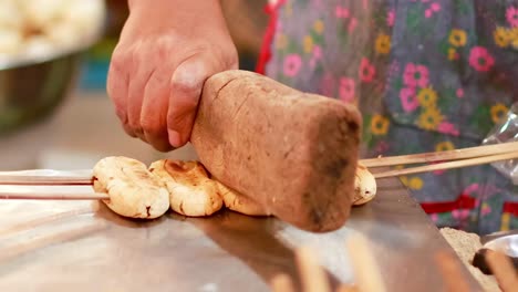 close-up of bananas being flattened on skewers using a wooden tool, highlighting the grilling process.