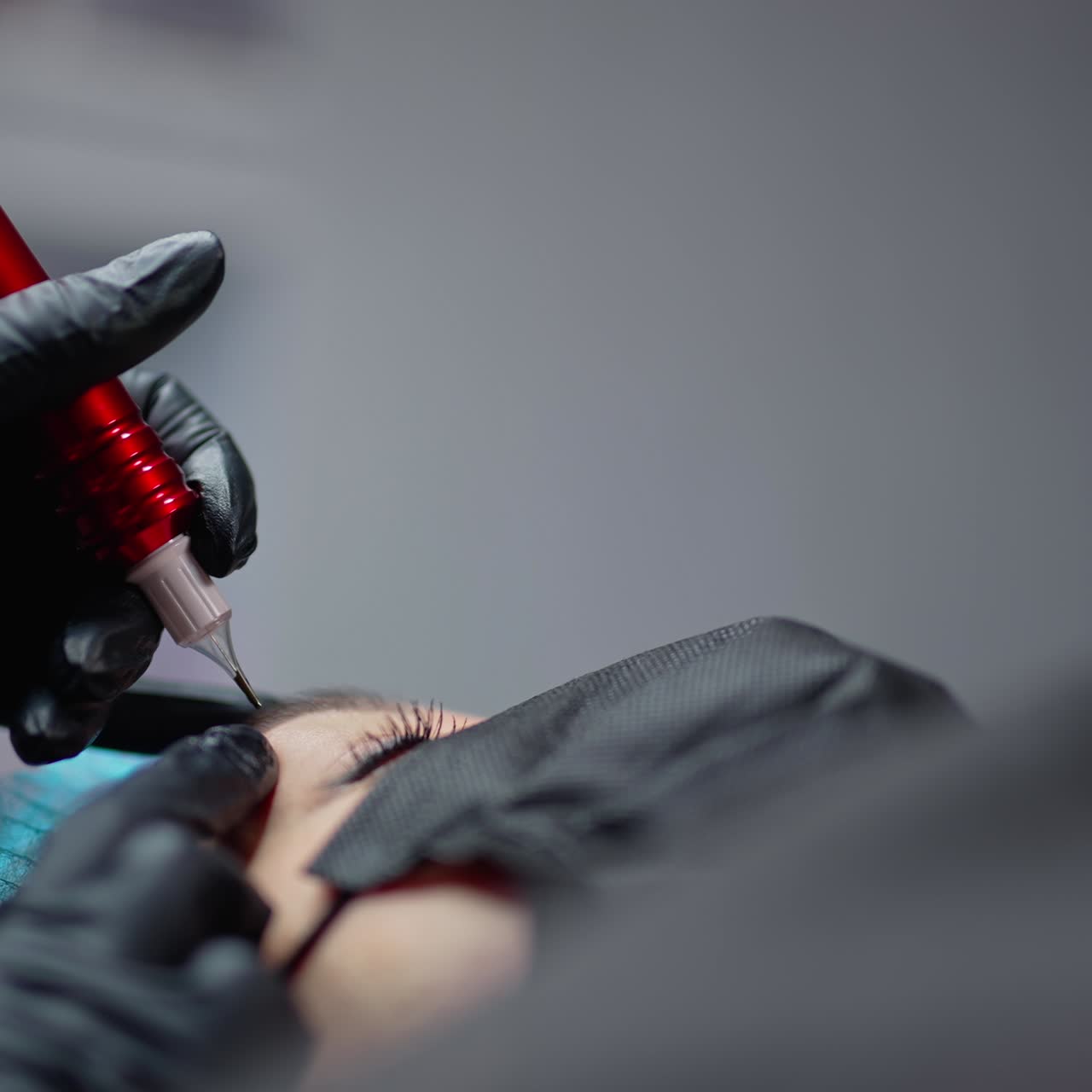 Black instrument for permanent make-up in the hand of professional cosmetologist in black gloves. Young woman is getting permanent lips make-up. Close-up