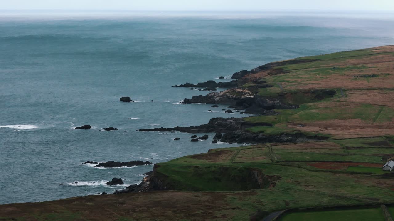 แสงอาทิตย์สาดส่องผ่านเมฆ ขณะที่ทุ่งหญ้าสีเขียวจรดมหาสมุทรที่ Dunquin