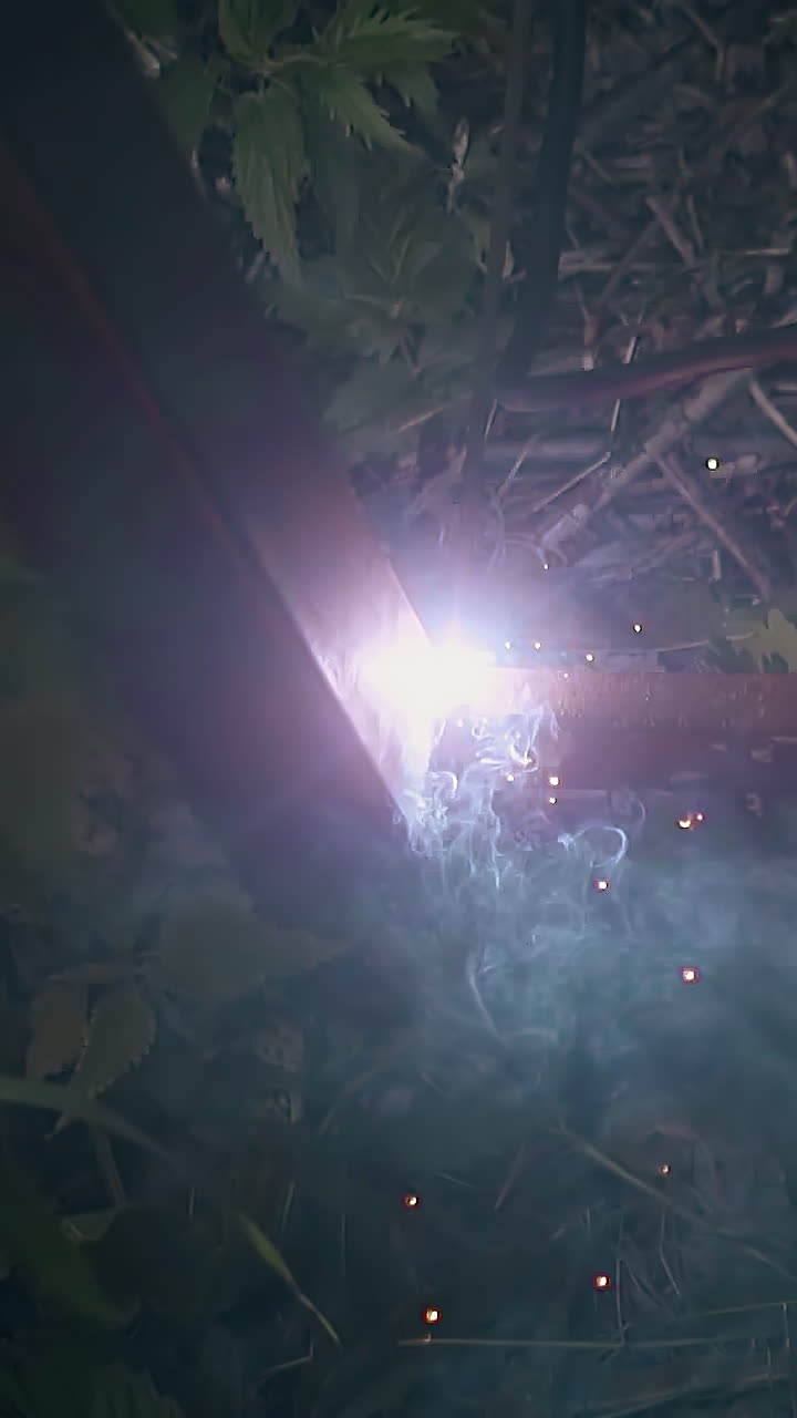 slow motion close view craftsman fixes bottom part to country house fence pole using welding machine