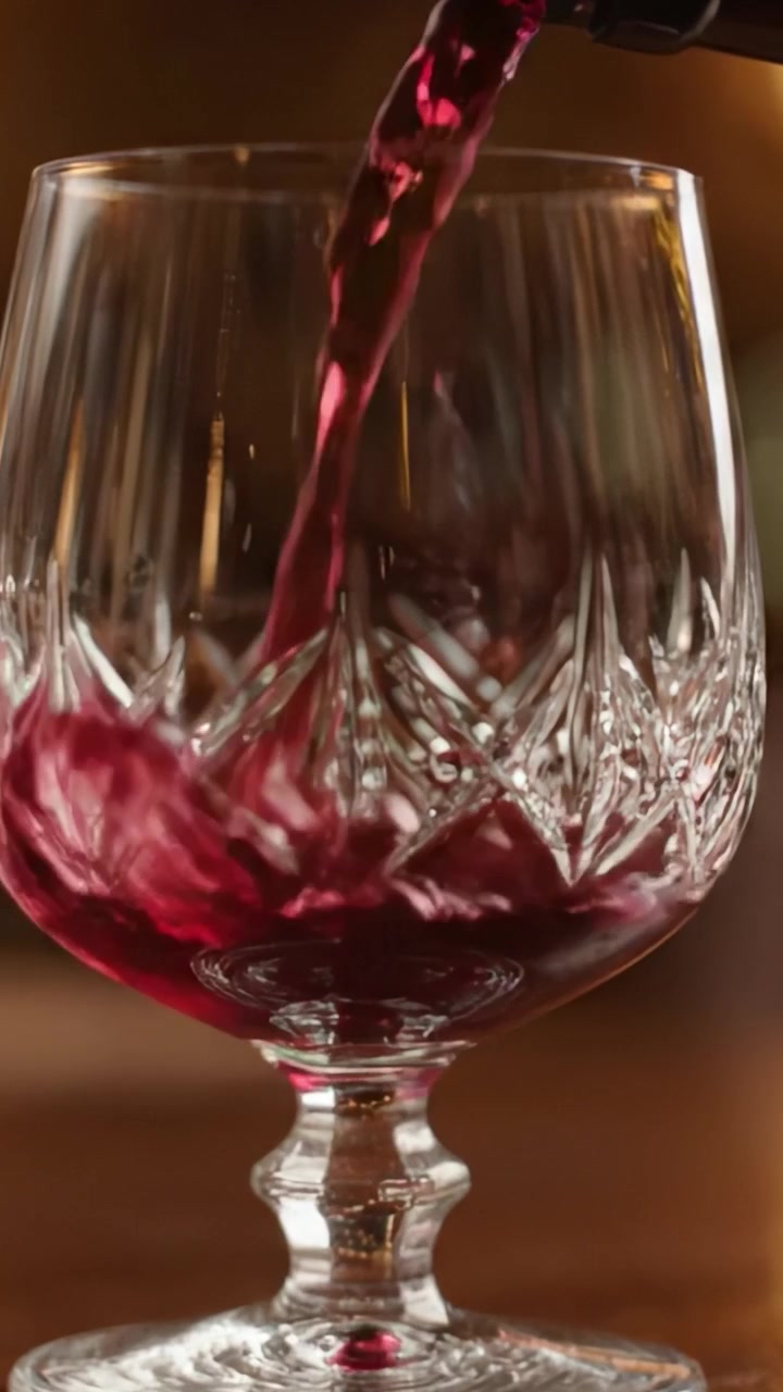 Un elegante bicchiere di cristallo riempito con ricco vino rosso, che mostra motivi intricati e superfici riflettenti in un ambiente sofisticato.
