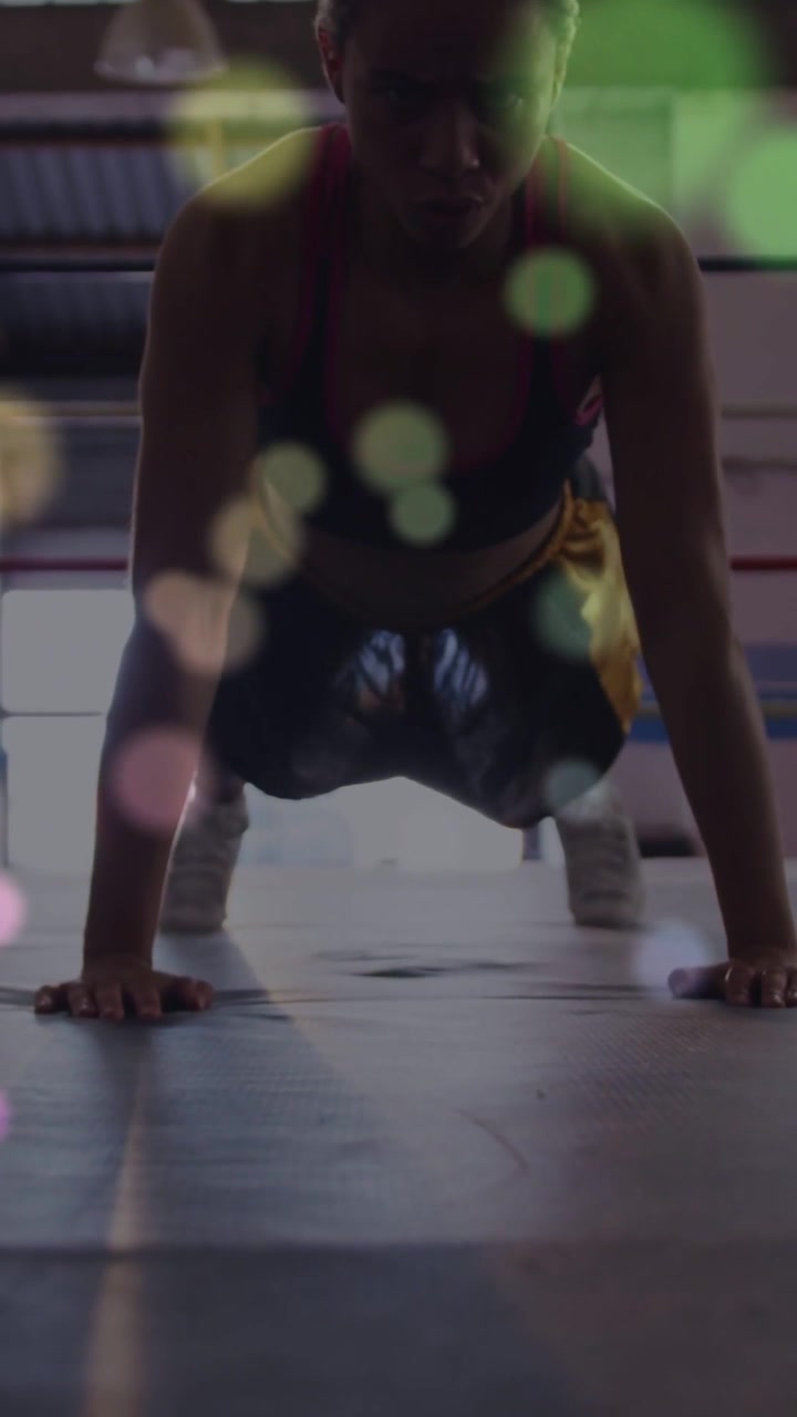 Video verticale: Pugile donna che si alza da una posizione bassa, spingendo verso l'alto per la boxe sul tappeto con un bagliore su di lei.