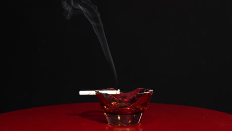 smoking cigarette isolated on dark background, burning in ashtray, quit smoking concept