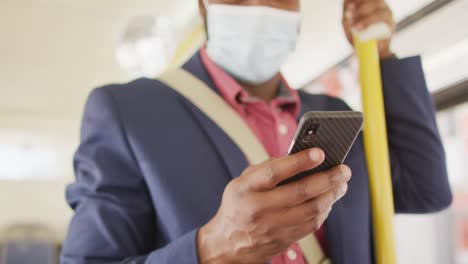 Hands-of-african-american-man-in-city-wearing-face-mask,-using-smartphone-in-bus