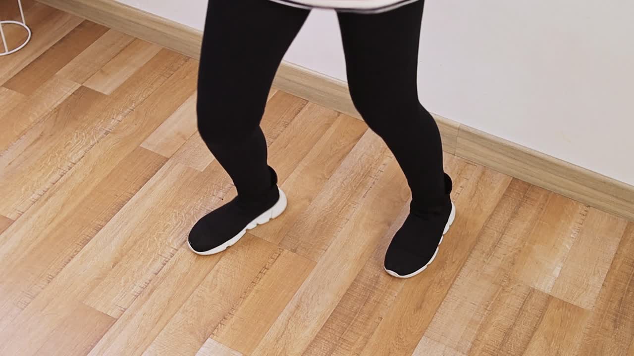 Close-up of person in black leggings and sneakers performing dance steps on wooden floor