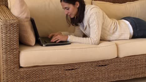 Fröhliche-Frau,-Die-Sich-Mit-Einem-Laptop-Auf-Dem-Sofa-Hinlegt