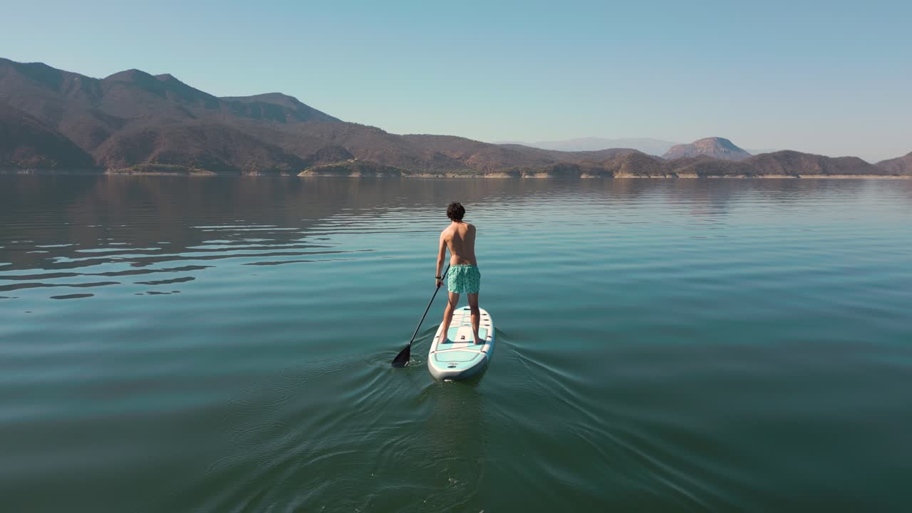 Homme faisant du paddleboard sur un lac calme avec des montagnes en arrière-plan
