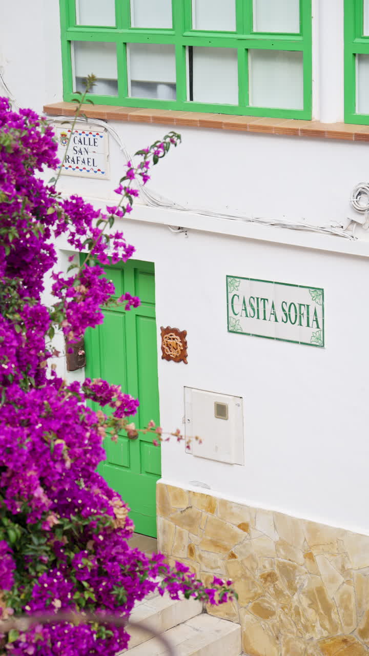 Alicante, Spain - May 20, 2025: Clean facade with green door and Casita Sofia sign on Calle San Rafael with pink flowers. Vertical