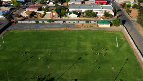 Aerial-drone-shot-of-boys-playing-a-game-on-a-green-rugby-field-in-the-middle-of-a-community-residential-area