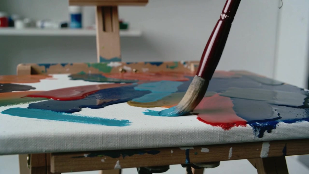Punta del pennello che si avvicina, carica di pittura turchese, che tocca la tela sul cavalletto, favorendo la miscelazione dei colori