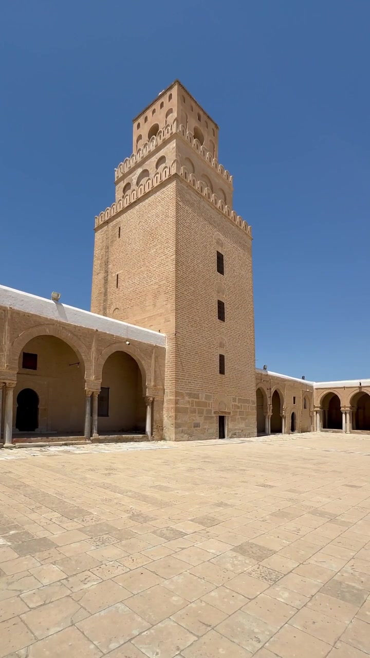 Antico cortile di moschea e torre del minareto a Kairouan, Tunisia, sotto un cielo azzurro e limpido.