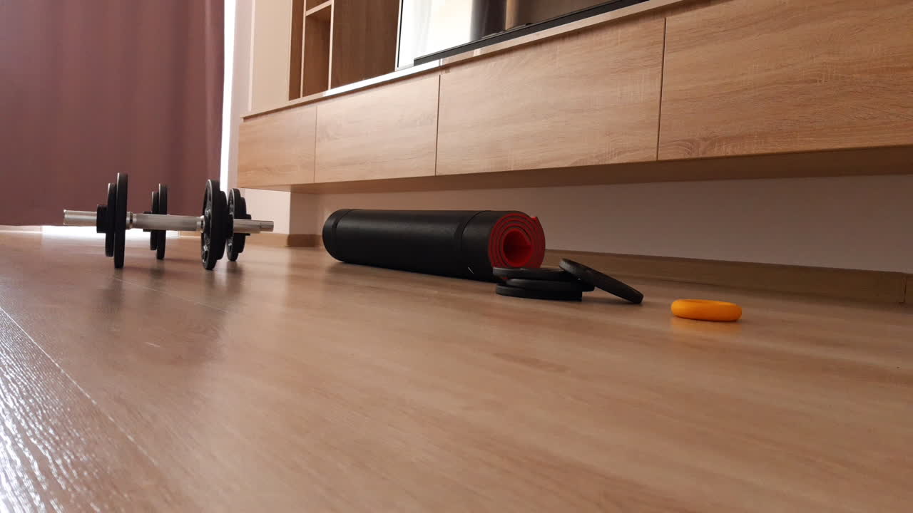 Two metal dumbbells roll on the living room floorstraight to the camera. Workout and exercises at home.