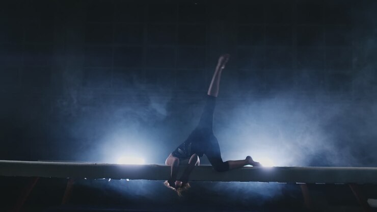 Women's Artistic Gymnastics. In slow motion in the smoke, the girl performs complex elements of the Olympic program on a balance beam.