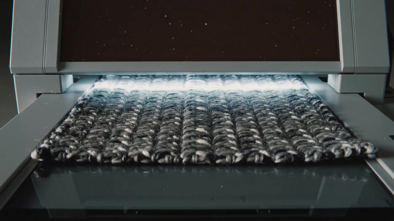 Machine pulling woven fabric swatch forward on glass bed after platen opening, showing LED platen