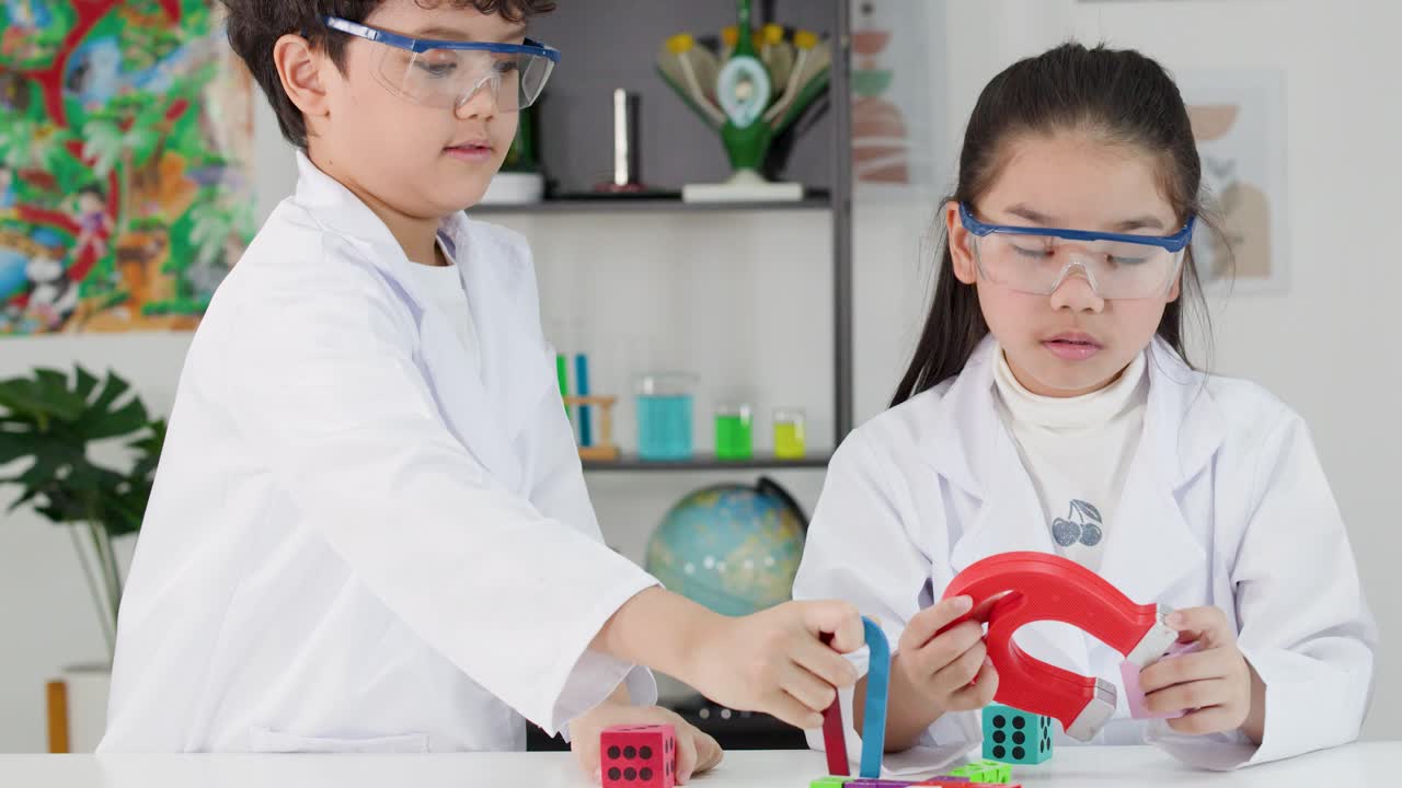 Siswa Asia yang fokus mengenakan kacamata pengaman saat menguji daya tarik magnet dengan magnet tapal kuda warna-warni