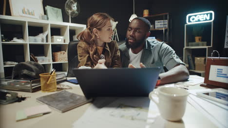 friendly girl talking to afro guy about data on laptop screen in workplace.